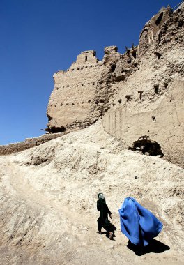 Afganistan, Gazni 'deki Gazni kalesinin duvarından bir kız ve kadın geçiyor. Kadın mavi bir burka (burka) giyiyor, orta Afganistan 'da geleneksel. Burka (burka) giymiş Afgan kadınlar.