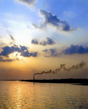 Khulna, Bangladeş yakınlarındaki Rupsa Nehri 'nde (Rupsha Nehri) gün batımı. Khulna ve Sundarban Ormanı arasındaki nehirde çekilmiş. Doğanın ve bacanın zıtlığı çevresel hasarı gösteriyor.
