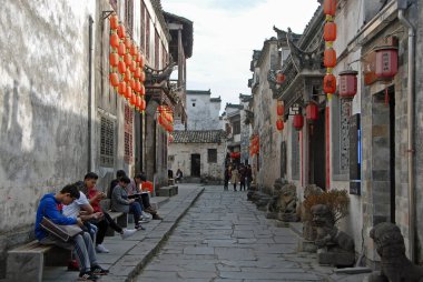 Xidi Ancient Town in Anhui Province, China. Old town of Xidi with historical buildings, cobbled street and red lanterns. Local people sit as tourists explore the historic town of Xidi. clipart