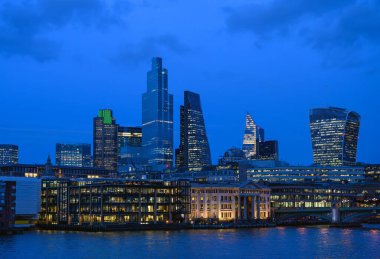 İngiltere 'deki Londra şehri. Akşamları Thames Nehri üzerinden Londra şehrine bakın. CBD 'nin gökdelenleri, ışıkları, nehri ve geceleri bulutlu mavi gökyüzü manzarası. Londra, İngiltere 2020.