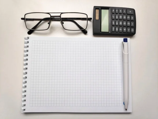 Gözlüklü ve hesap makineli bir not defteri. Beyaz bir masada..