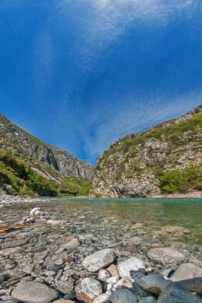 Balkanlarda bir dağ nehrinin kayalık kıyıları tüylü bulutlu mavi gökyüzüne karşı. Dikey manzara. Karadağ.
