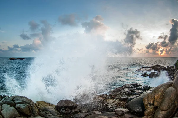 Waves break on the rocks at sunset. The sun breaks through the clouds. A fountain of spray falls on the rocks. Sri lanka.
