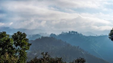 Dağlarda sisli bir sabah. Güneş ışınları yoğun bulutları zar zor aşıyor. Sri Lanca.
