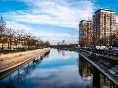 Dambovita nehri. Binalar, ağaçlar ve mavi gökyüzü suya yansıyor. Bükreş güneşli bir günde.