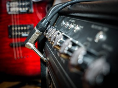 Gitar kablosu ve arka planda kırmızı gitarlı bir amplifikatör..