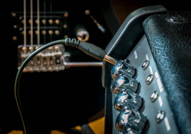 Fişi takılı bir yükseltici ve arka planda siyah bir gitar..
