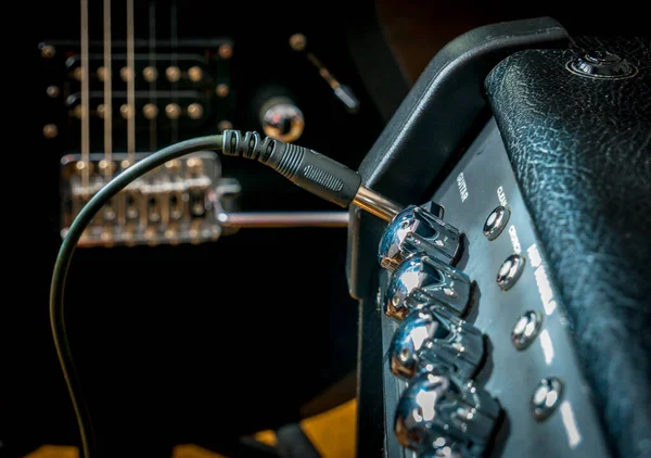 Fişi takılı bir yükseltici ve arka planda siyah bir gitar..