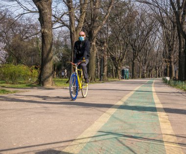 Bükreş / Romanya - 03.19.2020: Yüz maskesi takan bir adam bisikletten kurtuluyor. Koronavirüs pandemik koruması.