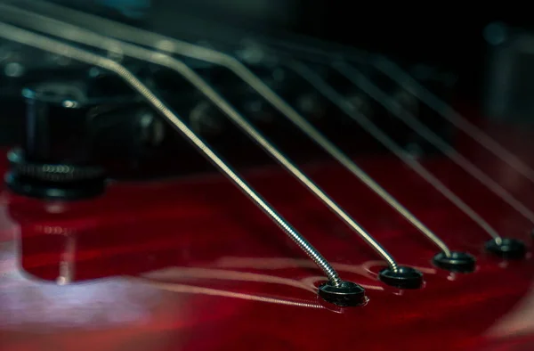 Close up with a guitar bridge and strings. Red guitar with blurred background.