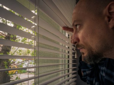 Pencere perdelerinden bakan tecrit edilmiş bir adam. Coronavirus salgınının yol açtığı kısıtlamalar sonucu adam evde kalmaya zorlandı..