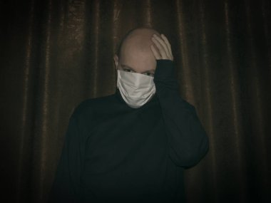 Kendini koronavirüsten korumak için yalıtılmış bir yüz maskesi takan kel bir adam. Bunalımlı adam başını tutuyor.