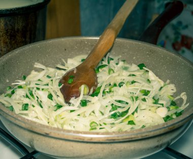 Tavada soğan dilimleri ve kızartılmaya hazır ahşap bir kaşık. Gaz ocağında yeşil soğan ya da Scallion..