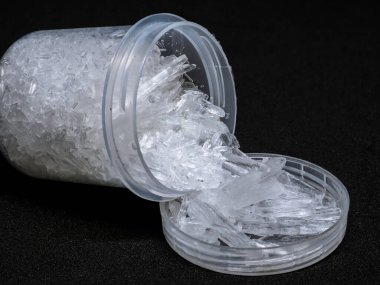 Siyah arka planda doğal mentollü kristaller. Mentollü kristallerle doldurulmuş küçük plastik alıcı.
