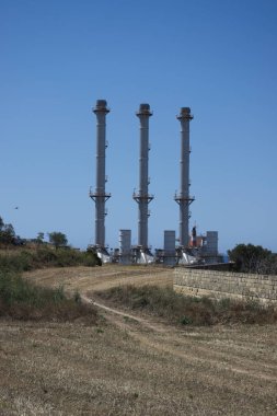 Akdeniz manzarasında mavi gökyüzüne karşı bacaları olan fabrikaya giden yol..