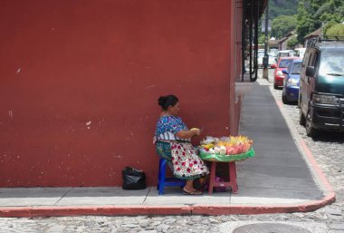 Antigua, Guatemala - Ağustos 2019: Kadın sebze satıcısı gölgede plastik sandalyede otururken yemek hazırlıyor.