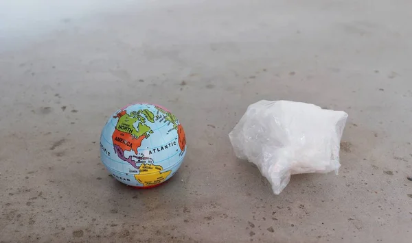 Plastik kirliliğini gösteren buruşuk bir plastik topun yanındaki dünya küresi..