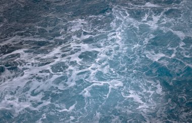 Mavi okyanus dalgaları beyaz köpüklü girdaplar oluşturuyor..