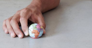 Ön taraftan görünen gri beton arka planı olan parmaklar tarafından tutulan küçük bir küre. Dünya ellerimizde ironik bir şekilde korunuyor..
