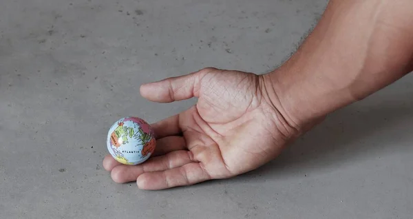 Small globe on hand with grey concrete background seen from the side. World in our hands with enironmental conservation.