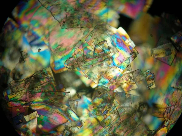 Crystallized liquid crystal under polarized light microscope forming a rainbow texture. Abstract squares filled with rainbow colors.