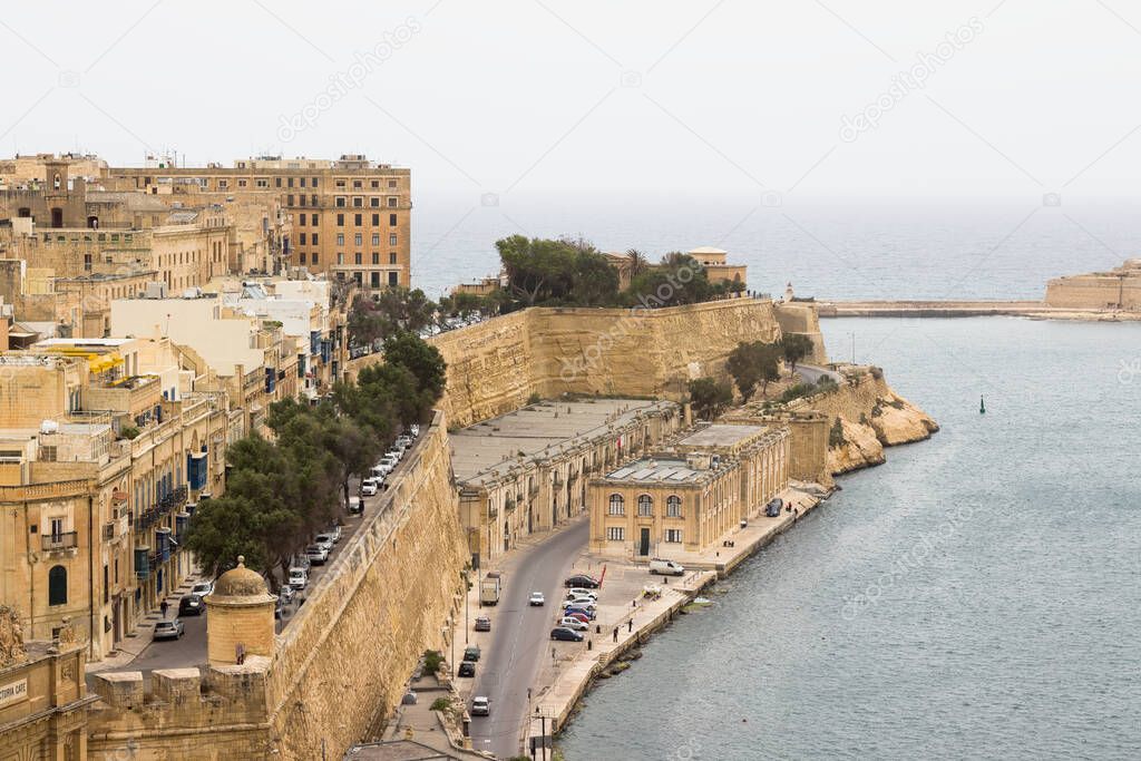 Skyline of Valleta with typical houses and beige limestone walls next to ocean.