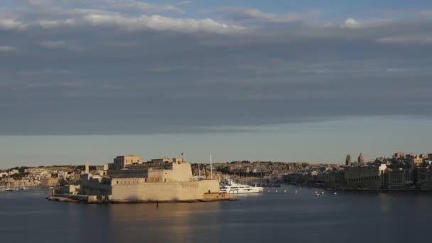 Vittoriosa, Malta 'da gün batımında. Güneş ışığı kalenin üzerinden geçiyor ve tekneler kanalda geziniyor.. — Stok video