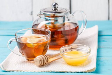 Bir bardak limonlu çay, cam çaydanlık ve mavi ahşap masada bal..