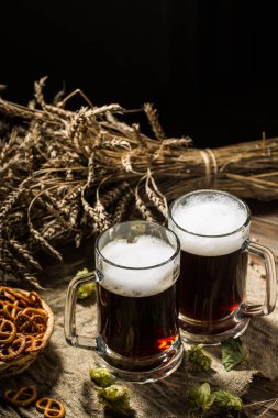 Buğday ve zıpzıp dolu iki tankard birası, ahşap masada bir sepet kraker.