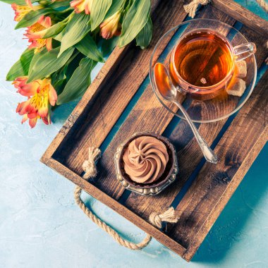 Hafif kahvaltı, siyah çay, kremalı kek ve tahta tepside portakal çiçekleri.