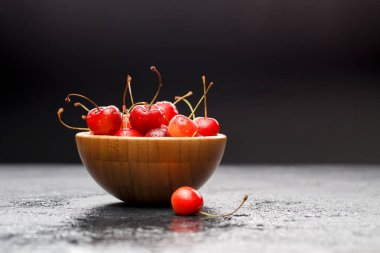 Gri masadaki ahşap bardakta tatlı vişne resmi.