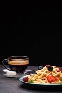 Çilekli Belçika gofretleriyle kahve fotografı, boş siyah arka planda ahududu.