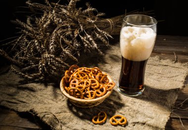 Buğdaylı cam bira ve ahşap masadaki keten kumaşlı kraker sepeti.