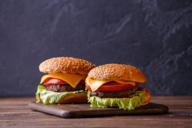 Siyah arka plandaki ahşap masada iki hamburger resmi.