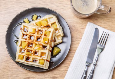 Ev yapımı waffle, mandalina, çikolata ve bir fincan kahve ve çatal bıçaklı siyah tabak.