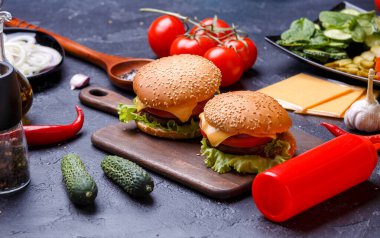 Tahtada iki hamburger, peynirli, domatesli siyah masa.