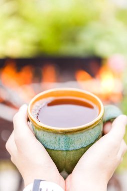 Elleri çay fincanı, brazier ve arkasında ateş tutuyordu.