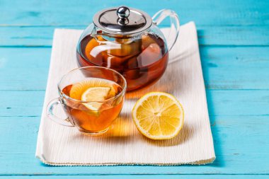 Mavi ahşap masada limonlu ve cam çaydanlıklı bir bardak çay..