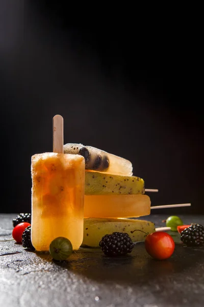 Photo of fruit ice from berries on stick, blackberry, cherry, gooseberry on black background