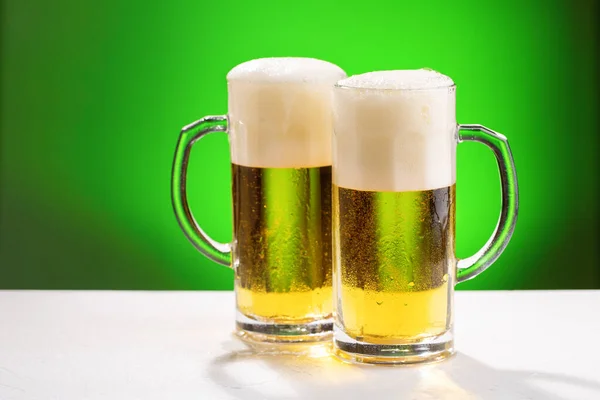 Two mugs of beer on white table. Concept for St. Patrick\'s day.
