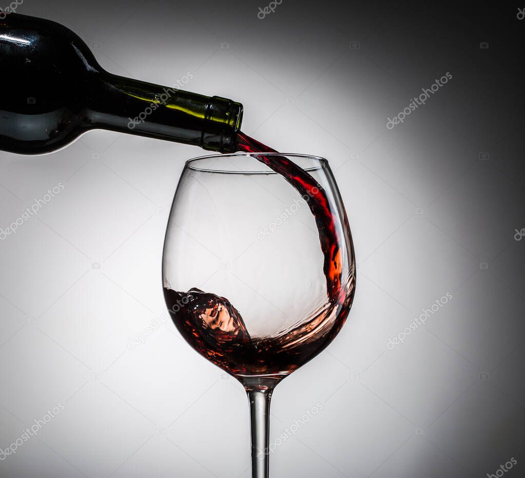 Grape wine poured from bottle into wine glass from glass on blank background