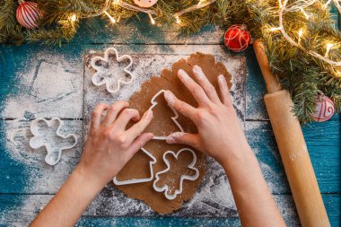 İnsan eli fotoğrafı, merdane, hamuru, ladin dalları, çelenkler, mavi masadaki bisküvi kalıpları.