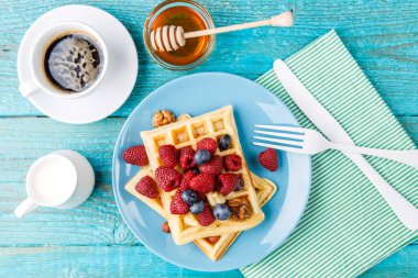 Homemade waffles with raspberries and blueberry, cup of coffee, milk and cutlery. Tasty breakfast clipart