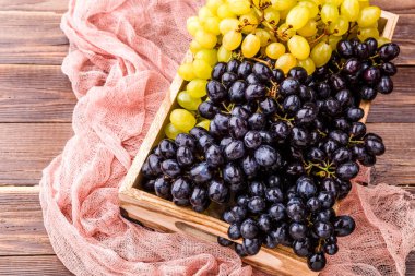 Stüdyoda masasında pembe bez olan tahta kutuda siyah üzüm resmi.