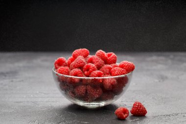 Siyah arka planda şeffaf cam bardakta taze ahududu resmi