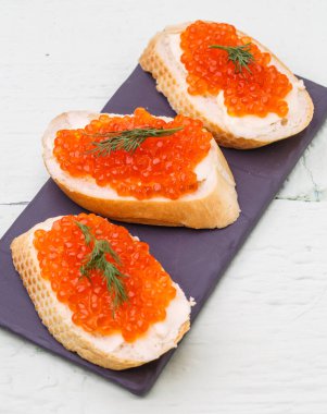 Beyaz ahşap masada kırmızı havyarlı sandviçlerin fotoğrafı.