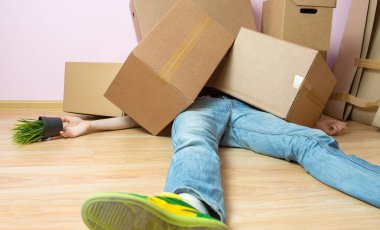 Yeni dairede karton kutuların altında yatan kot pantolonlu bir adam resmi