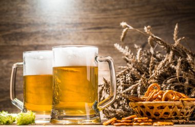 Boş ahşap arka planda bira köpüklü fincanlar, krakerler, zıpzıp ve buğdaylar.