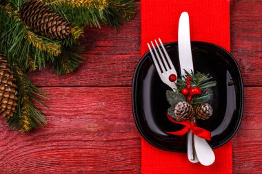 Kırmızı peçete, siyah tabak, beyaz çatal ve bıçakla süslenmiş ökseotu ve Noel çamı dallarıyla Noel masası. Yeni Yıl Saat Sembolü. Noel tatili geçmişi.