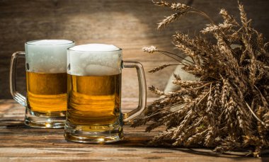 Boş ahşap arka planda iki kupa birayla buğday dikenleri